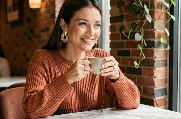 Boucles d'oreilles géométriques dorées et bagues sculptées portées par une femme dans un café parisien