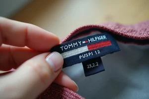 Gros plan sur une étiquette Tommy Hilfiger authentique tenue entre les doigts pour vérifier les détails de broderie et éviter les contrefaçons