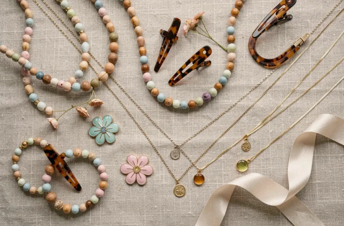 Flat lay tendance de bijoux fantaisie variés sur tissu lin incluant colliers, broches émail et clips en acétate